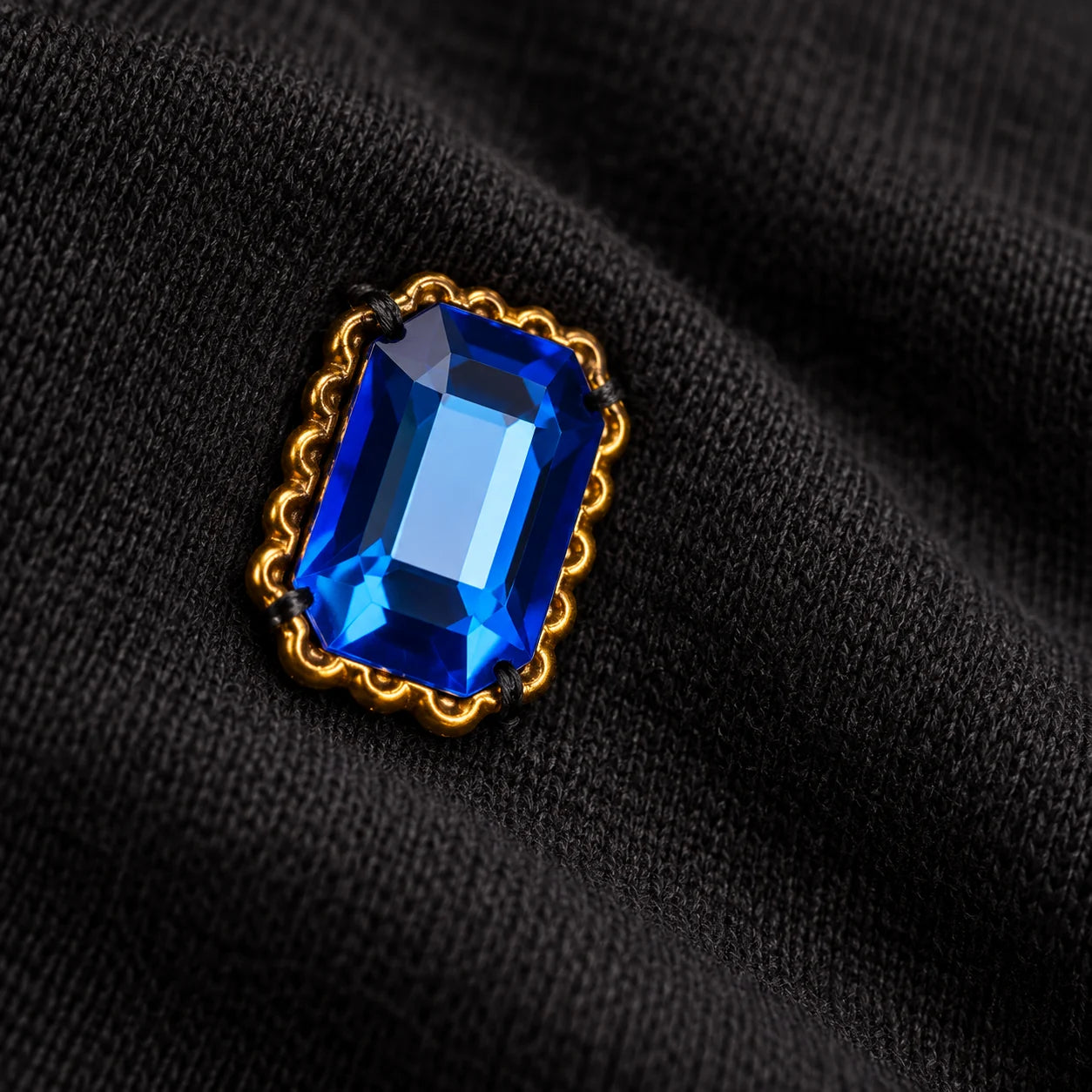 Illustrative close-up of a blue decorative stone and its stitched attachment on black cotton